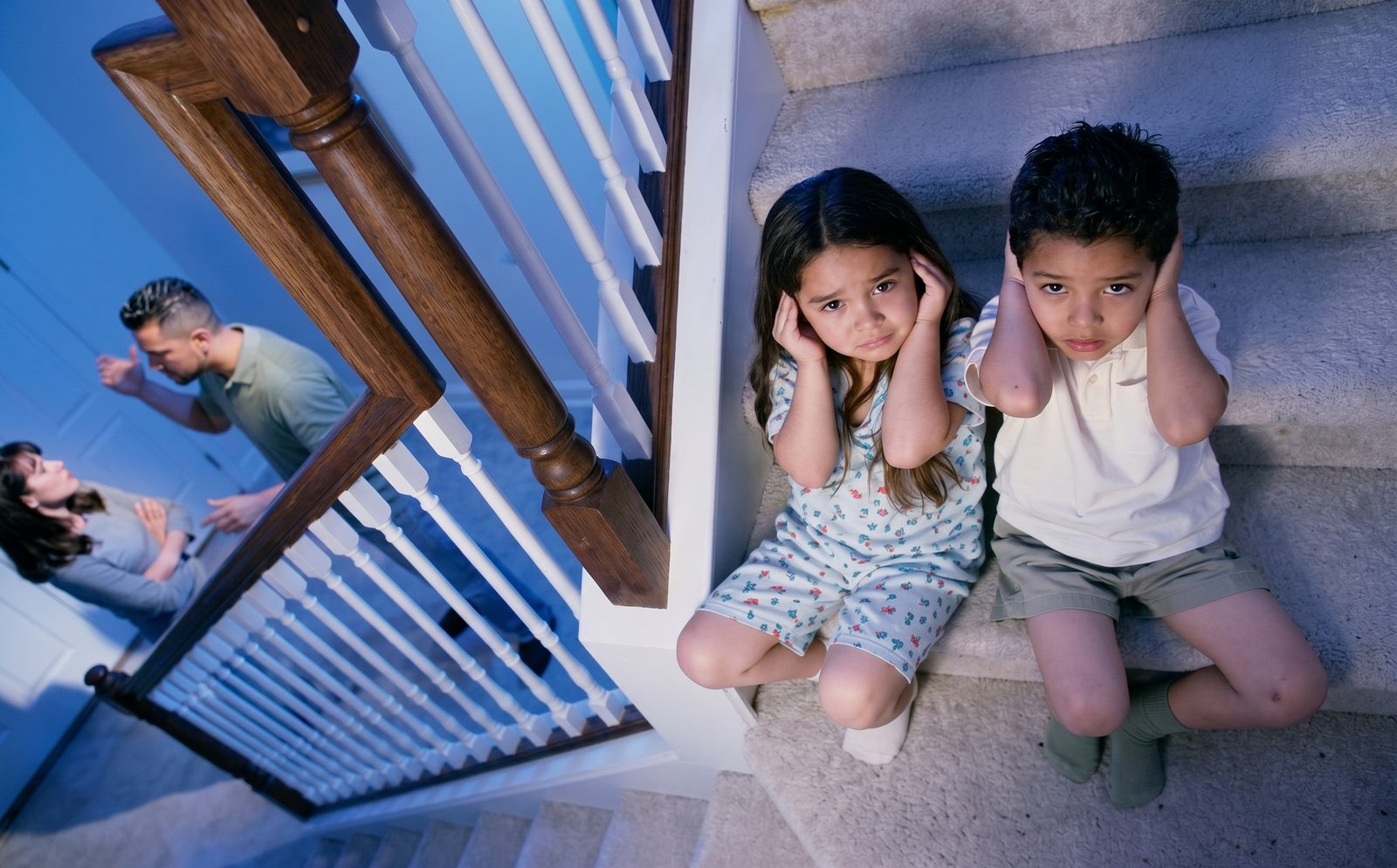 Dos niños sentados en las escaleras se tapan los oídos mientras sus padres discuten